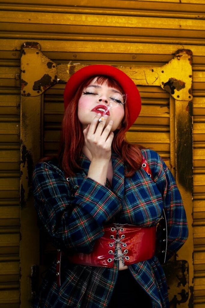 A striking fashion portrait of a woman in a red beret and plaid coat against a yellow industrial background.